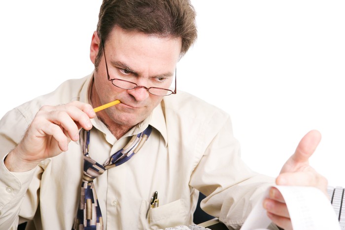 An accountant chewing on a pencil while closely analyzing figures from his printing calculator.